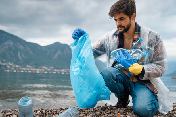 istock Unhappy young man holding garbage bag and putting plastic bottles from beach 1526217319