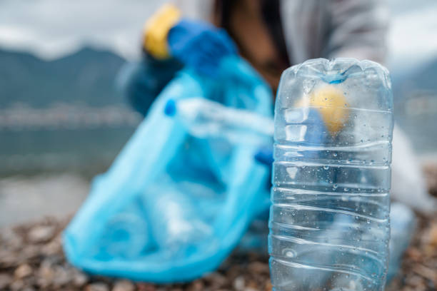 istock Closeup of empty plastic bottle while unknown person in the background is cleaning the beach 1526217859