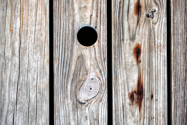 Full frame close-up view of wooden planks exposed to the weather screwed to make either a deck floor or a fence containing a peep hole.
