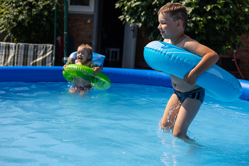 Children laugh and jump in an inflatable pool on a sunny summer day. Children escape from the heat in the cool water of the pool. Happy childhood concept..