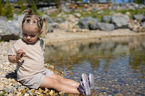 Small girl in pastel clothes running along the riverbank with a reed in hand. Fun concept