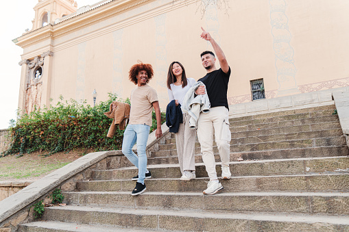 Group of diverse multiethnic student people walking together downstairs of the campus, talking, pointing and smiling. Young teenage asian woman with two male friends having a conversation after class. High quality photo