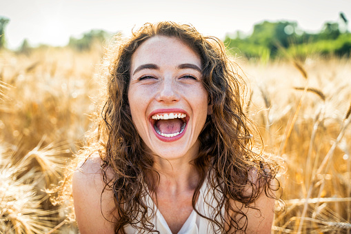 Happy beautiful woman smiling in a wheat field - Delightful female enjoying summertime sunny day outside - Wellbeing concept with confident girl laughing in the nature
