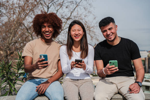 Group of multiracial teenage friends having fun using a cellphone device outdoors. Three multiethinc young people smiling and laughing watching a mobile phone sharing on social media at the street. High quality photo grupo de estudiantes adolescentes sonrientes multirraciales sosteniendo un teléfono celular y mirando a la cámara. tres amigos felices y diversos usando un teléfono inteligente. jóvenes multiétnicos divirtiéndose usando una aplicación de teléfono m