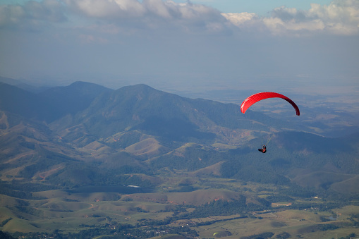 red Paraglider flying over valley on a clear day with blue sky.