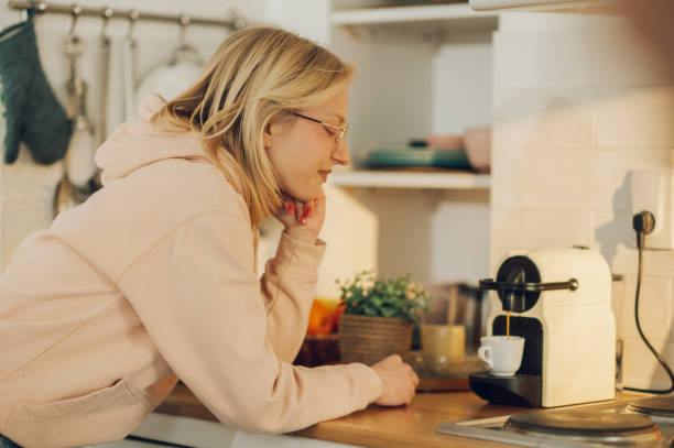 zaspana kobieta czeka na przygotowanie porannej kawy, stojąc w kuchni w domu. - snow making machine zdjęcia i obrazy z banku zdjęć
