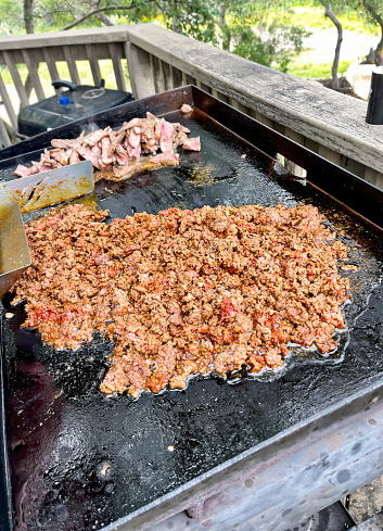 Ground beef sizzles in seasonings and grease as it is cooked outdoors for tacos on a weekend afternoon.