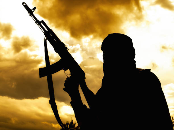 Muslim militant with rifle in the desert on sunset uder heavy clouds stock photo