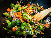 Delicious healthy vegetarian stir fry dish with broccoli, carrots and cabbage in a cast iron wok pan with a wooden spatula.