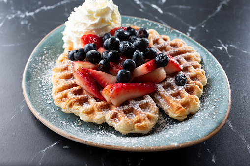 A view of a croffle, featuring fresh berries and whipped cream.