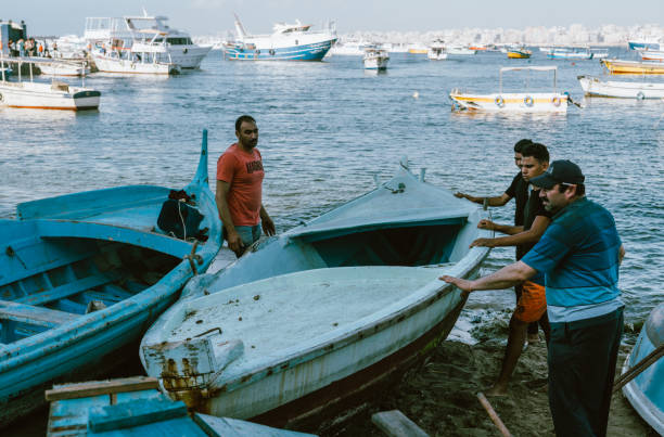 Alexandria, Egypt - June 21, 2023:Fisherman working at coast of Mediterranean Sea in Alexandria Harbor. The cityscape of Alexandria and fisherman boats can be seen in the background.
