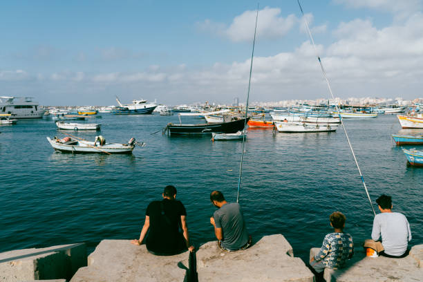 Alexandria, Egypt - June 21, 2023:Fisherman working at coast of Mediterranean Sea in Alexandria Harbor. The cityscape of Alexandria and fisherman boats can be seen in the background.