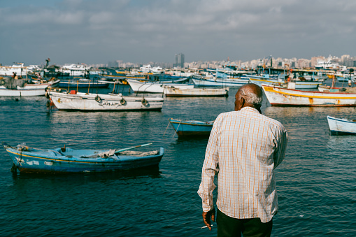 Alexandria, Egypt - June 21, 2023:Fisherman working at coast of Mediterranean Sea in Alexandria Harbor. The cityscape of Alexandria and fisherman boats can be seen in the background.