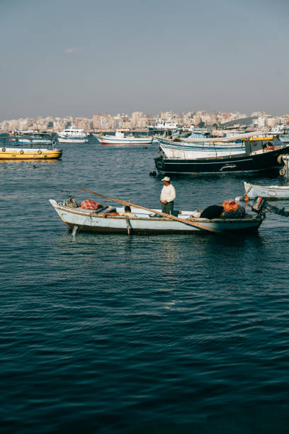 Alexandria, Egypt - June 21, 2023:Fisherman working at coast of Mediterranean Sea in Alexandria Harbor. The cityscape of Alexandria and fisherman boats can be seen in the background.