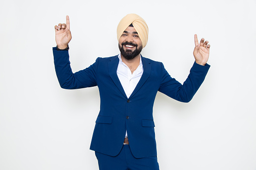 Cheerful indian sikh businessman wearing suit dancing with joy isolated over white background. Corporate Concept.
