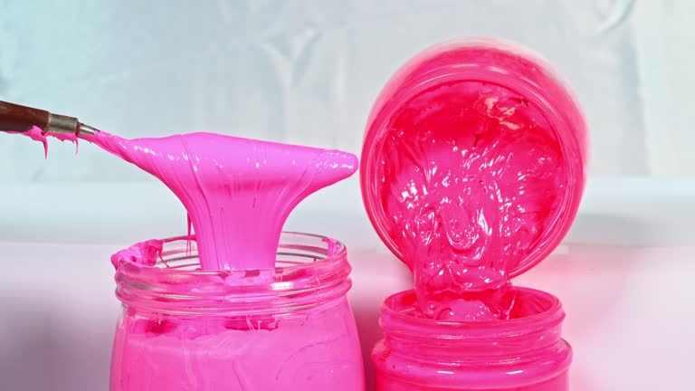 Use a trowel to stir the pink ink in a glass jar.