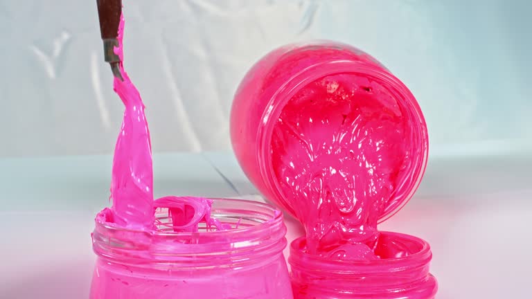 Use a trowel to stir the pink ink in a glass jar.