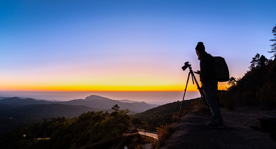 Silhouette Professional Photographer with camera take a landscape photo at twilight sunrise