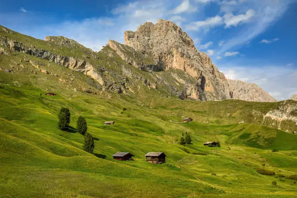 Wooden huts on the grassy hillside of the Seceda peak in the Italian Dolomites.
