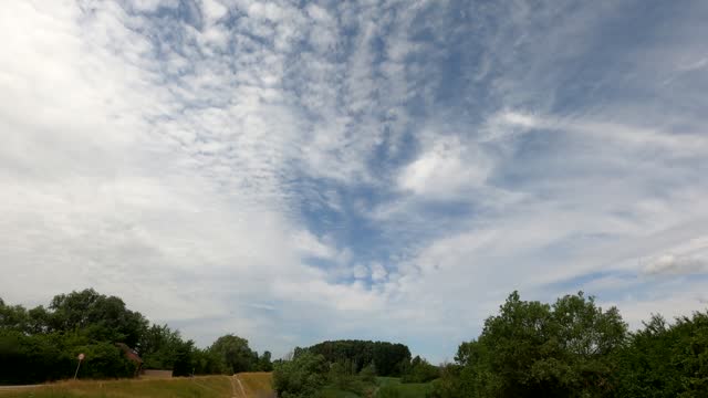 Altocumulus clouds in time-lapse mode and green summer meadow