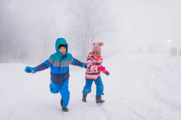 Winter portrait of a beautiful little boy and girl laughing and having a lot of fun in snow.
