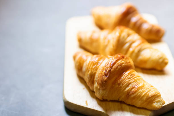 istock Fresh croissant on wooden board with nature sunlight through window. 1527420529