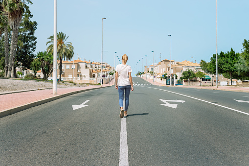 a european girl in a t-shirt and jeans walks along the road with her back to the camera, a beautiful cityscape with a girl