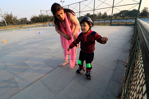 Elementary child of Indian ethnicity learning roller skating in sports ground with his mother portrait close up.