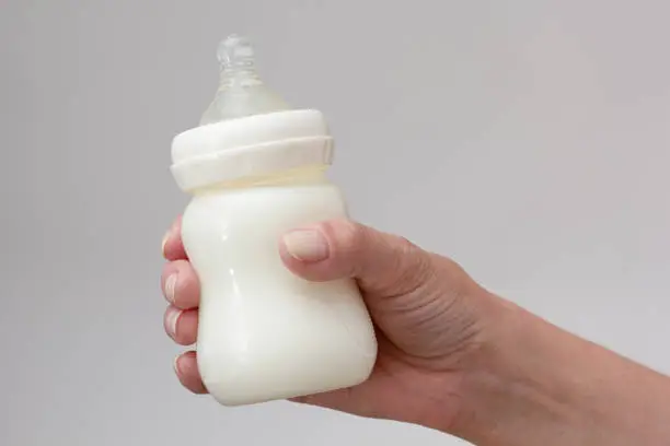 Isolated bottle feeding full of milk in cropped woman hand on white background