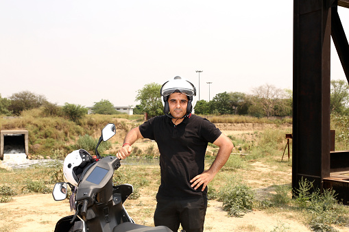 Mid adult traveler of Indian ethnicity standing portrait near electric scooter outdoor in nature.