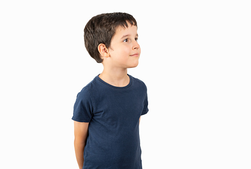 Child wearing casual t-shirt standing over white background looking away to side with smile on face, natural expression. Laughing confident.