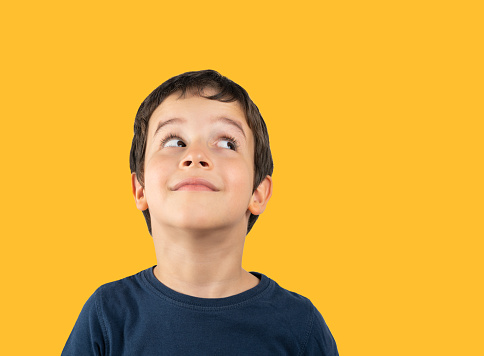 Child with blue shirt over isolated yellow background looking away to side with smile on face, natural expression. Laughing confident.