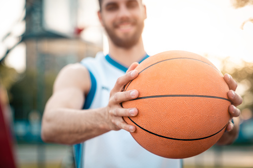 Close up selective focus photo of a basketball player holding a basketball in the forefront. Sport concept photography promoting healthy lifestyle. Sports ball. Focus on basketball. Sport Concept.