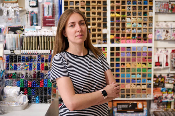 confident young woman, sales manager, seller looking at camera, standing with her arms folded in school stationery shop - sales clerk store manual worker retail imagens e fotografias de stock