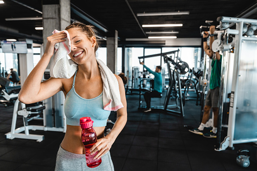 Happy athletic woman taking a break at the gym. Smiling attractive woman feeling tired but proud after successful training session.