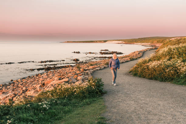 Mature woman walking along the coastline across from the Orkney Islands of Scotland in mid summer, just before the summer solstice. The view towards the Orkney Islands to the north gives that wonderful feeling of space where you just drift off into another universe.