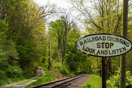 A railroad crossing sign next to tracks in the woods in Titusville, Pennsylvania, USA on a sunny spring day