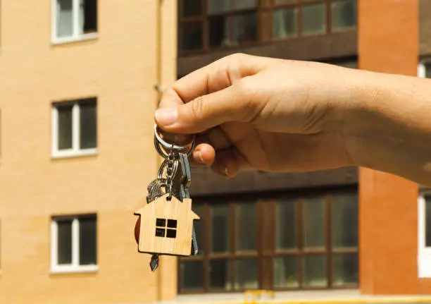 Photo of A woman holds the keys to a new quart or house. The keys open and close the door lock. The owner opens the door of a new house. The concept of selling and renting real estate.