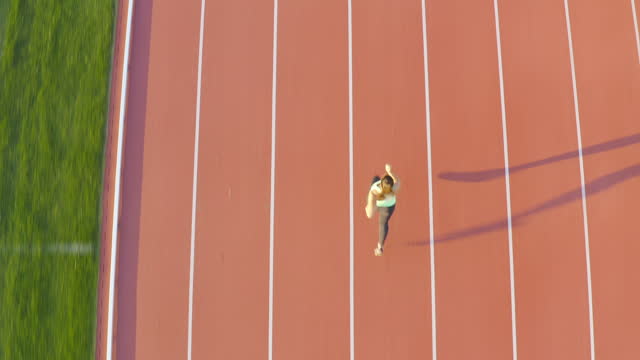 Female athlete alone on the athletic track, sprint running, aerial view