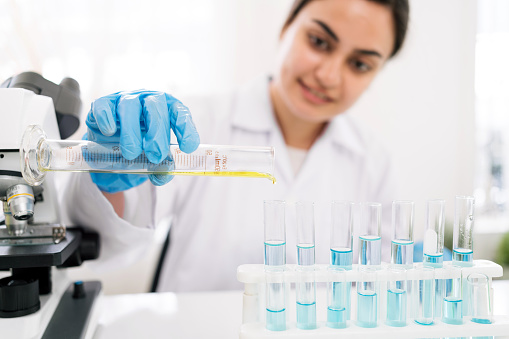 Middle East woman scientist researcher rinse liquid from a graduated cylinder to test tube for analysis of liquids in the lab. Scientist working with test tube and graduated cylinder.