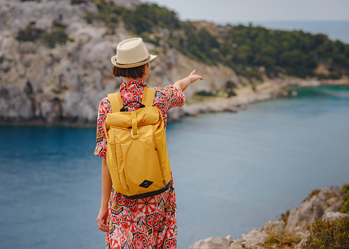 Asian woman in hat look on views of azure Bay in Mediterranean sea. Travel and vacation concept. Anthony Quinn bay with crystal clear water in Rhodes island, Greece. The most beautiful beach.