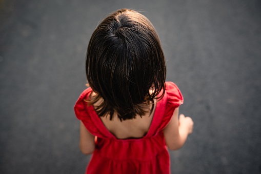 close up view of little girl in red dressstanding in the evening in the road