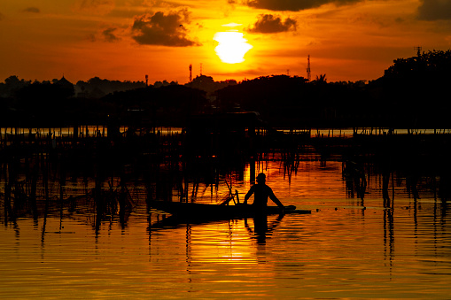 Aceh, Indonesia, July 6, 2023: A fisherman rowing a boat at sunset in a reservoir, in Lhokseumawe, Aceh Province, Indonesia, July 6, 2023.
