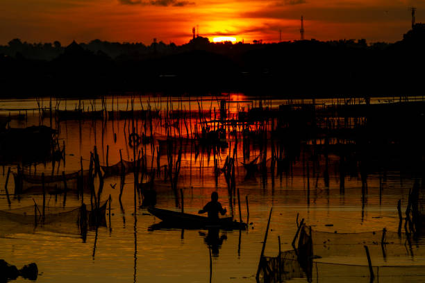 Aceh, Indonesia, July 6, 2023: A fisherman rowing a boat at sunset in a reservoir, in Lhokseumawe, Aceh Province, Indonesia, July 6, 2023.