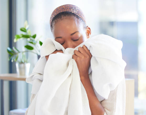 Linen, cleaning and fresh with a black woman smelling fabric or textile while working in a home as a cleaner. Laundry, housekeeping and scent with a female maid at work with soft sheets to smell