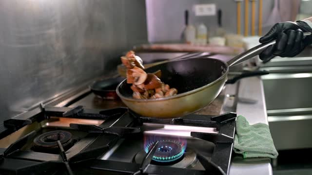 Slow motion of crop anonymous male cook flipping mushrooms and shrimps in frying pan while cooking appetizing food in restaurant kitchen