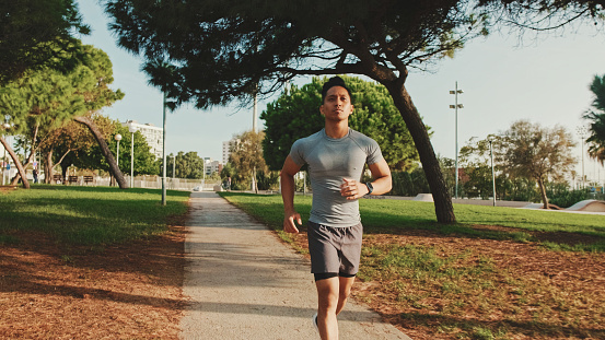 Guy in sportswear, an athlete on a morning run in a city park, jogging on a sunny day, a healthy lifestyle