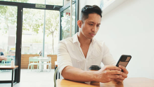 istock Young businessman sits at table with mobile phone and drinks coffee in cafe 1528133997
