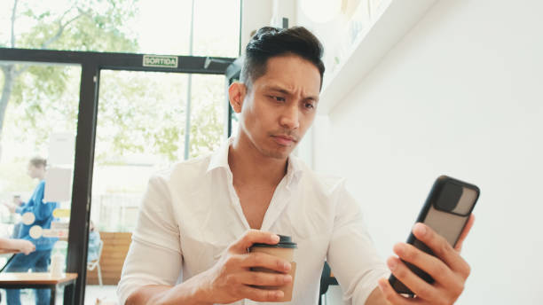 istock Young businessman sits at table with mobile phone and drinks coffee in cafe 1528133998