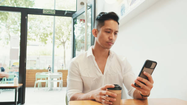 istock Young businessman sits at table with mobile phone and drinks coffee in cafe 1528134024